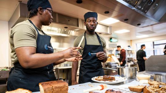 Private Amika Joseph (L) of 1 Medical Regiment and Trooper Akeem Woods (R) of the King’s Royal Hussars prepare their Banana and Chocolate cake for tasting by the Judges (Picture: British Army).