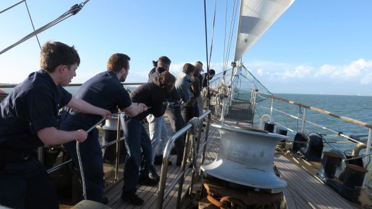 Sailors and ships company haul in a line on TS Tenacious