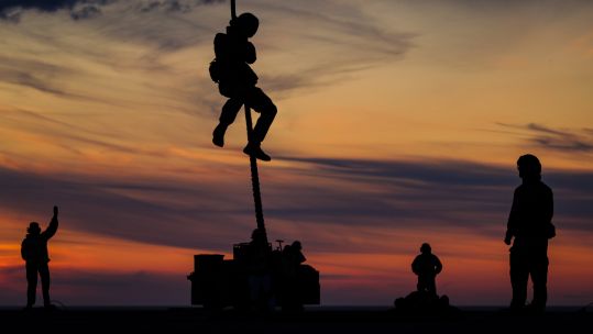 Silhouetted anonymous Royal Marines from Lima Company 42 Commando doing fast rope training (Picture: Royal Navy).