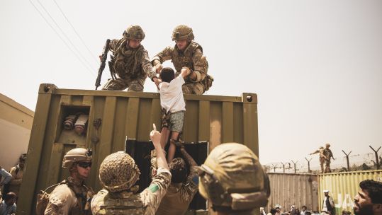 UK coalition forces, Turkish coalition forces, and US Marines assist a child during an evacuation at Kabul airport
