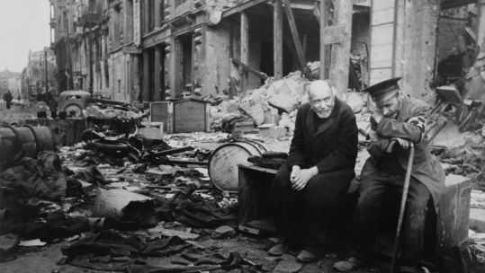 World War 2, Battle of Berlin, May 1945. Two elderly German men, one wearing the armband signifying blindness, the other his helper, sitting on a crate amid the rubble.