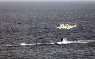 A Merlin Mk2 helicopter flies over HMS Agamemnon's tail fin as she conducts diving trials (Picture: Royal Navy)