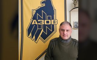 Jack Lopresti poses with an Azov Brigade banner with its eagle and wolfsangel symbols