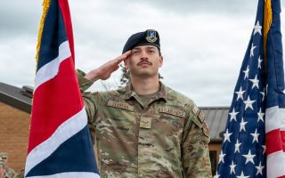 A US airman salutes the flags of the United Kingdom and the United States at RAF Fairford in Gloucestershire (Picture: US Department of War)